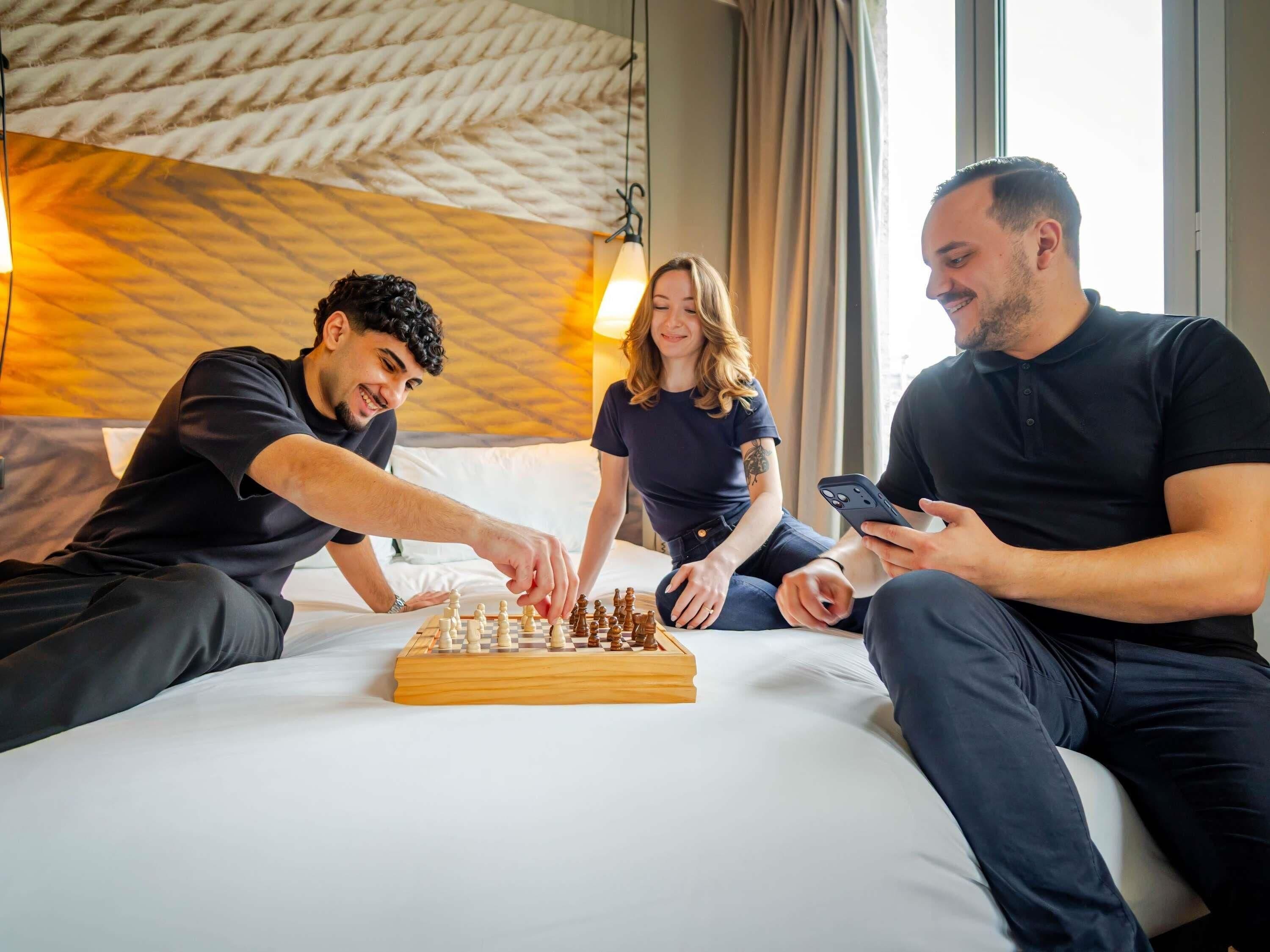 Een hotelkamer met een bed, een houten schaakbord en iemand die schaakt.