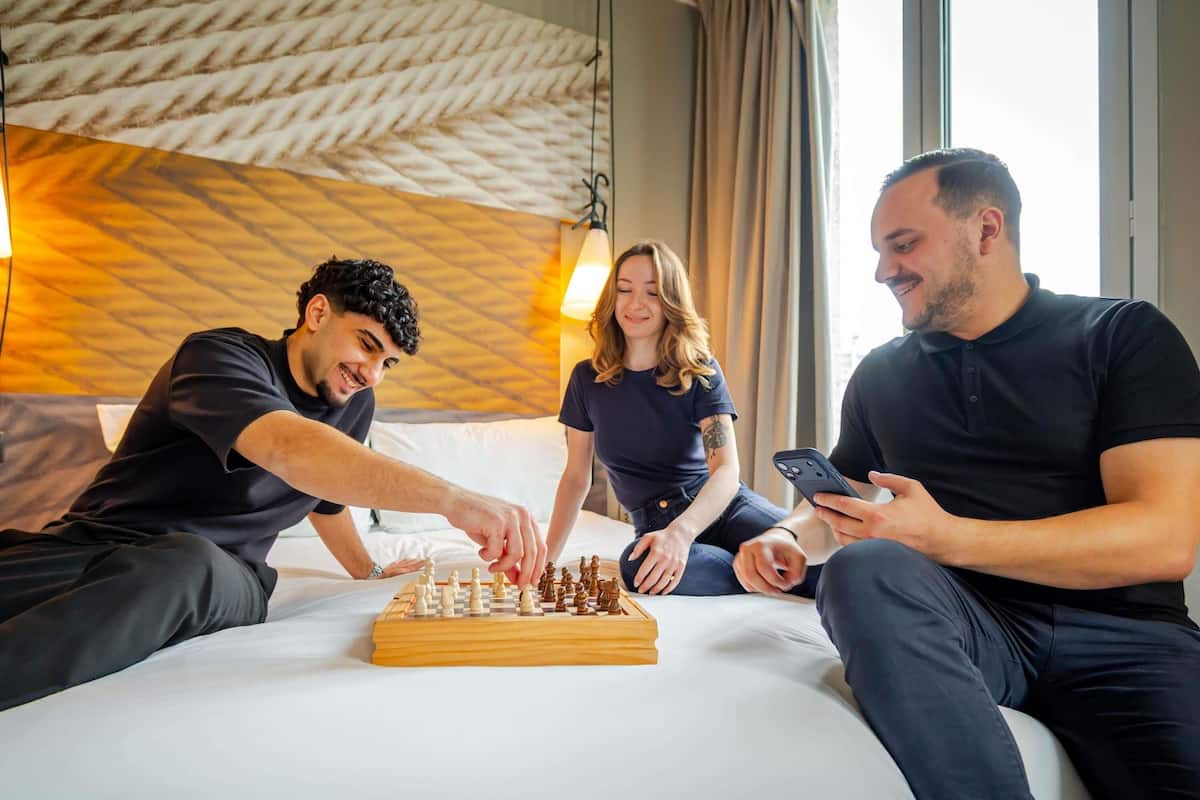 Een hotelkamer met een bed, een houten schaakbord en iemand die schaakt.