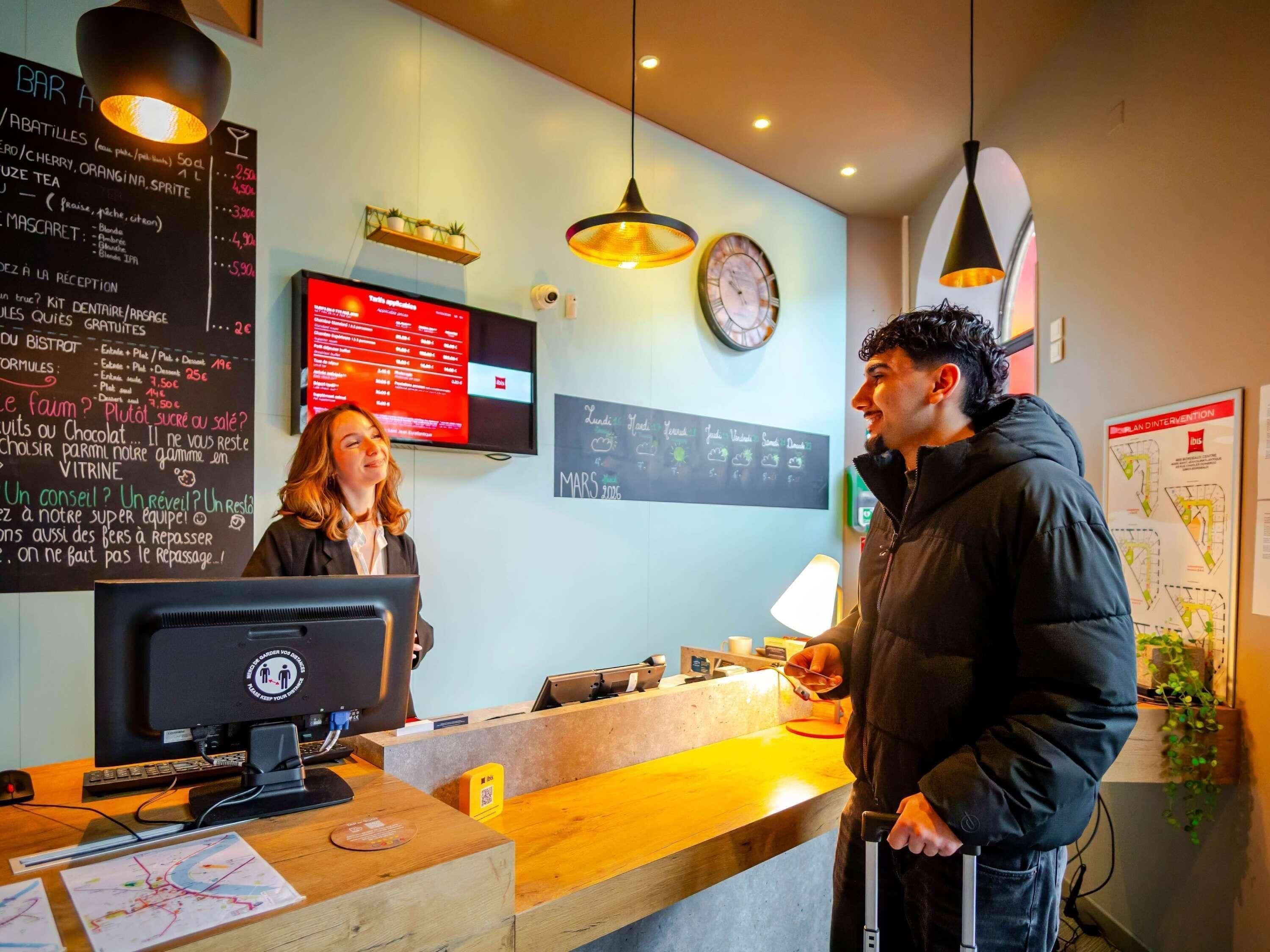 Un comptoir d’accueil avec un écran d’ordinateur, un tableau affichant le menu et une horloge au mur.