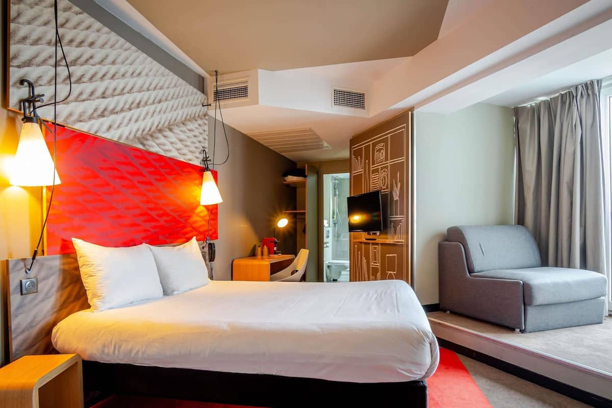 Hotelkamer met een bed, een bureau, een stoel, een televisie en een badkamer zichtbaar door een geopende deur.