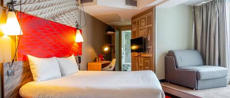 A hotel room with a bed, a desk, a chair, a TV, and a bathroom visible through an open door.