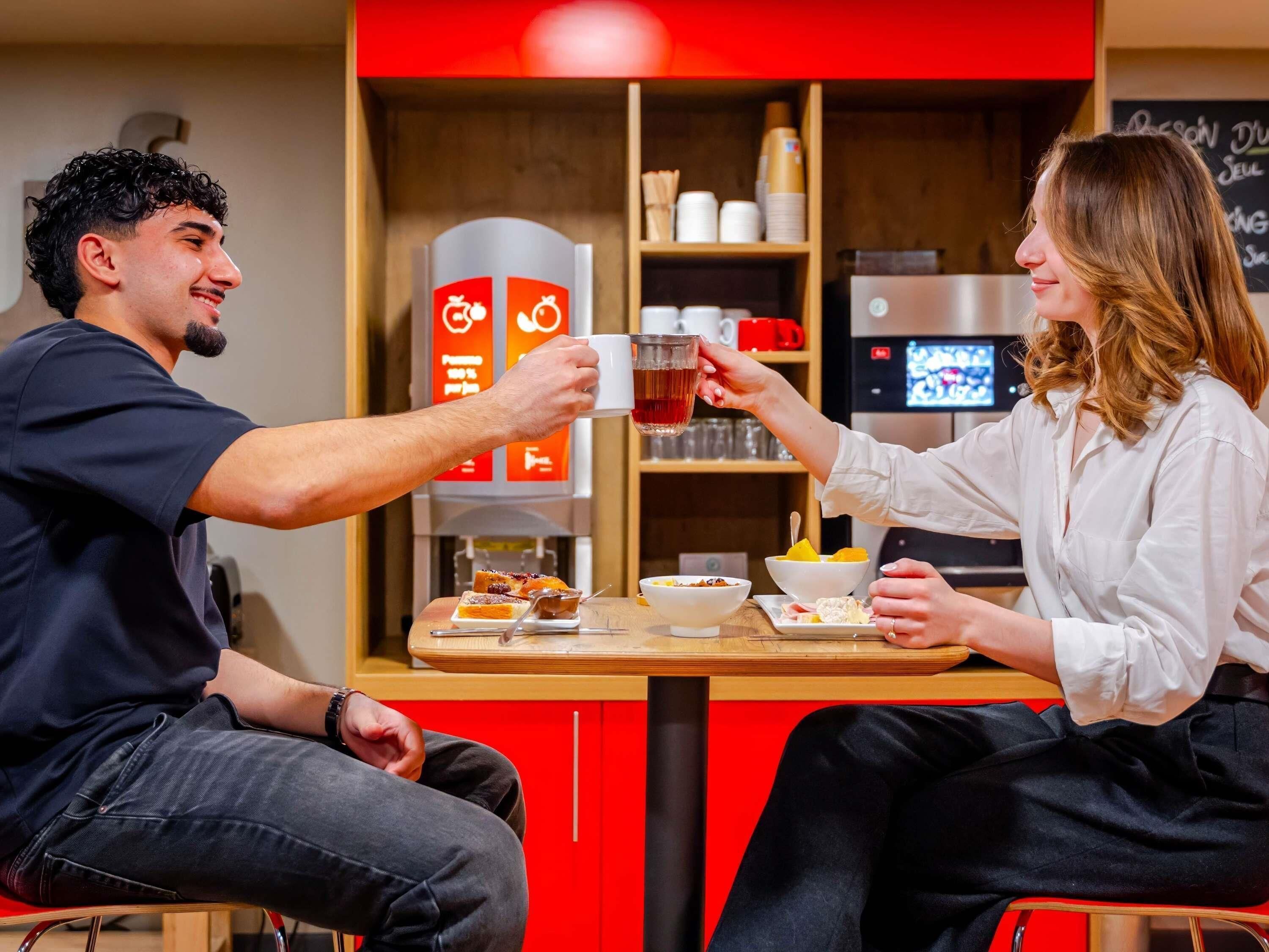 A person holding a mug, another person holding a spoon, and a table with food and a coffee machine.