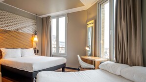 Una camera d'albergo con un letto, una scrivania, una sedia, una lampada e una finestra con tende.