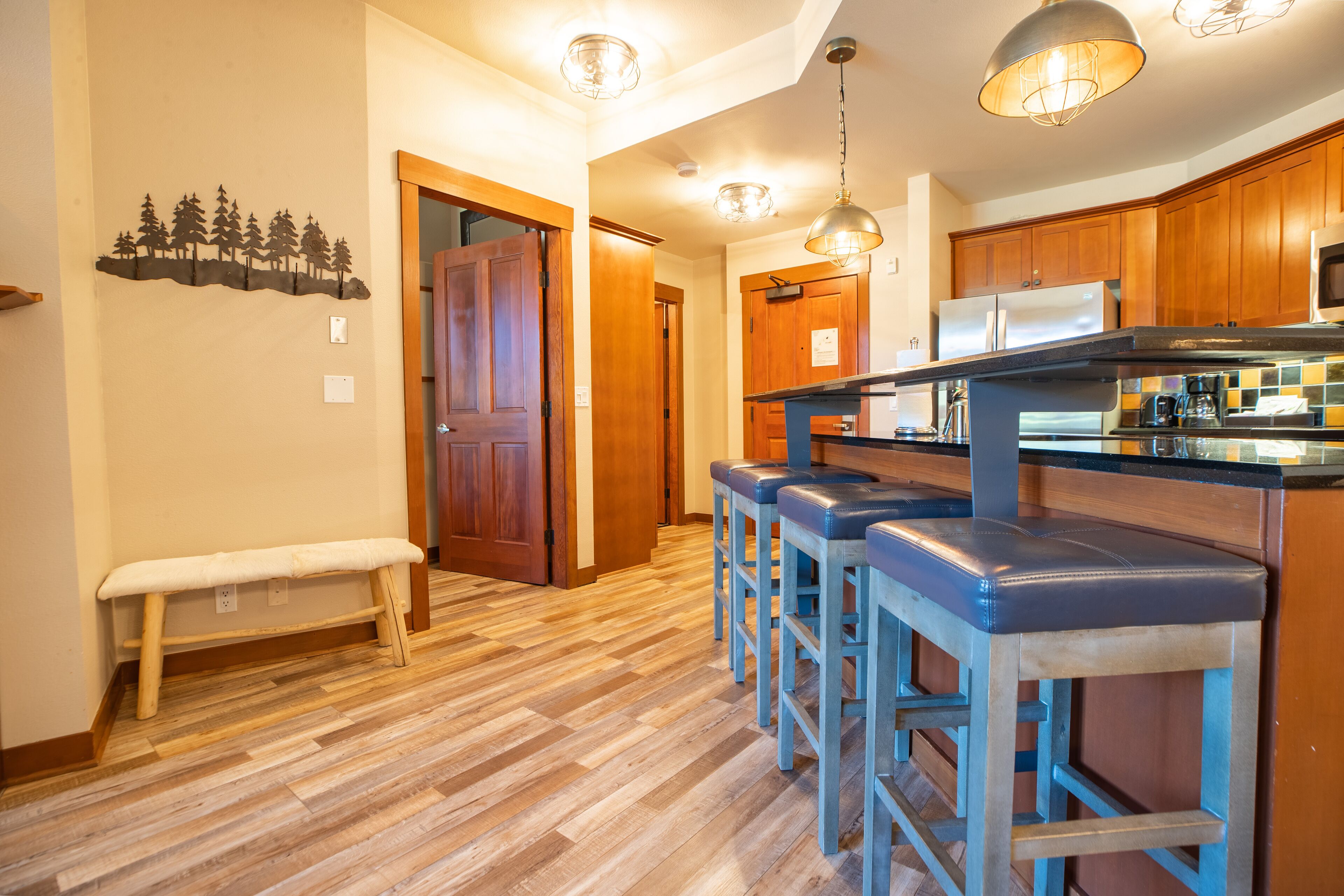 A kitchen with wooden cabinets, a stainless steel refrigerator, and a bar area with stools.