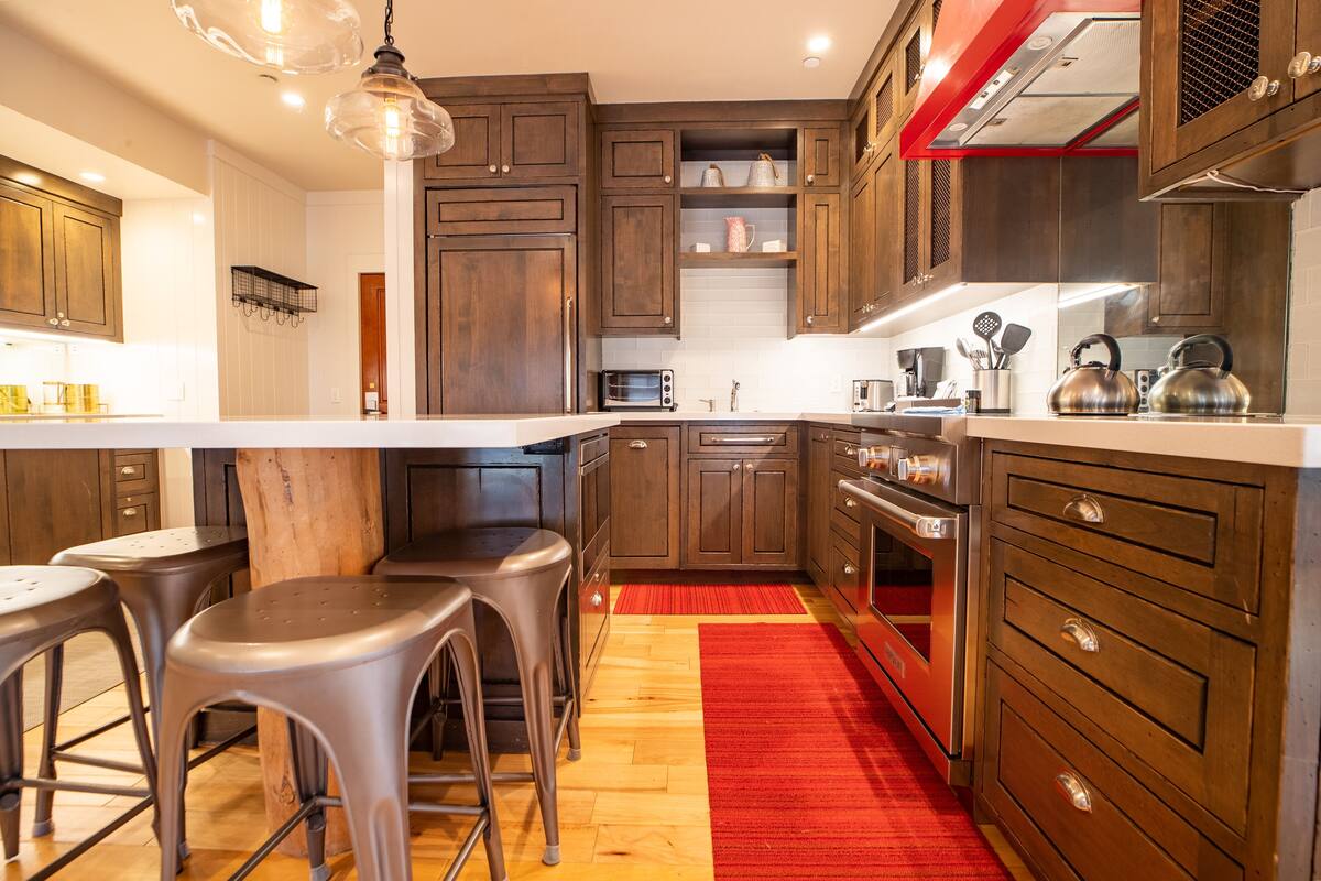 A modern kitchen with wooden cabinets, stainless steel appliances, and a red rug.