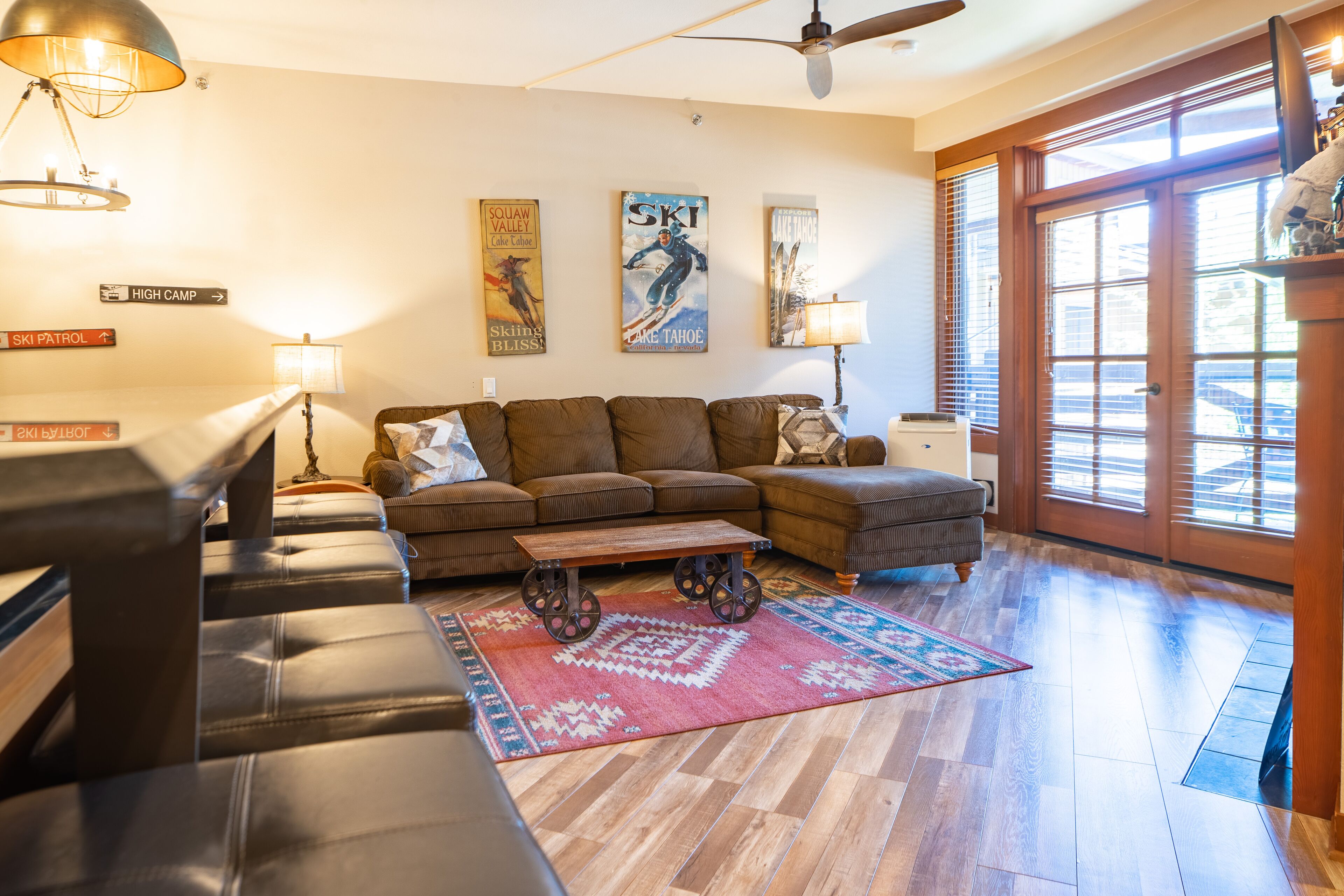 A living room with a sectional sofa, a coffee table with wheels, a patterned rug, and wall art depicting skiing.
