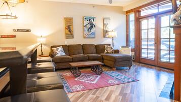 A living room with a sectional sofa, a coffee table with wheels, a patterned rug, and wall art depicting skiing.