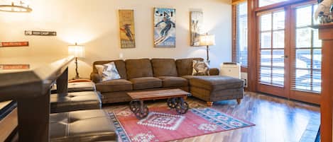 A living room with a sectional sofa, a coffee table with wheels, a patterned rug, and wall art depicting skiing.