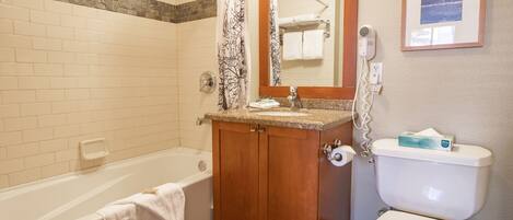 A bathroom with a bathtub, a toilet, a vanity with a sink, a shower curtain, and a framed picture on the wall.