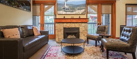 A living room with a stone fireplace, leather furniture, and a large TV mounted above it.