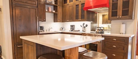 Cocina con armarios de madera, una isla grande con taburetes y electrodomésticos modernos.