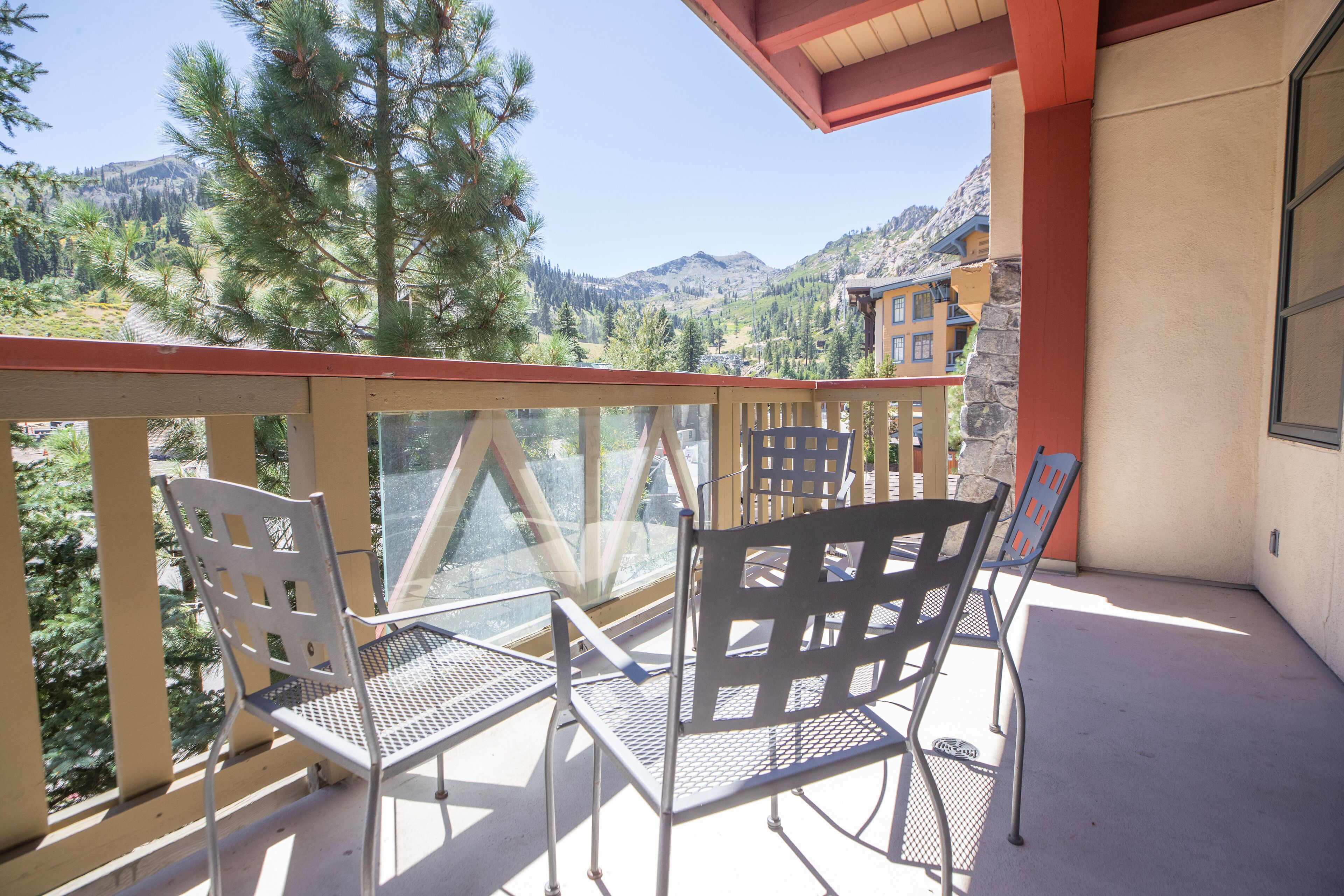 A balcony with metal chairs and a table, overlooking a mountainous landscape with pine trees and buildings.