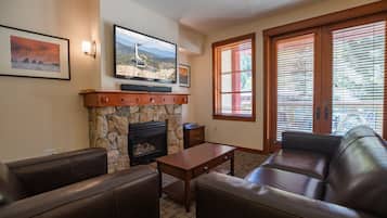 A living room with a stone fireplace, leather sofas, a wooden coffee table, and a flat-screen TV mounted above the fireplace.