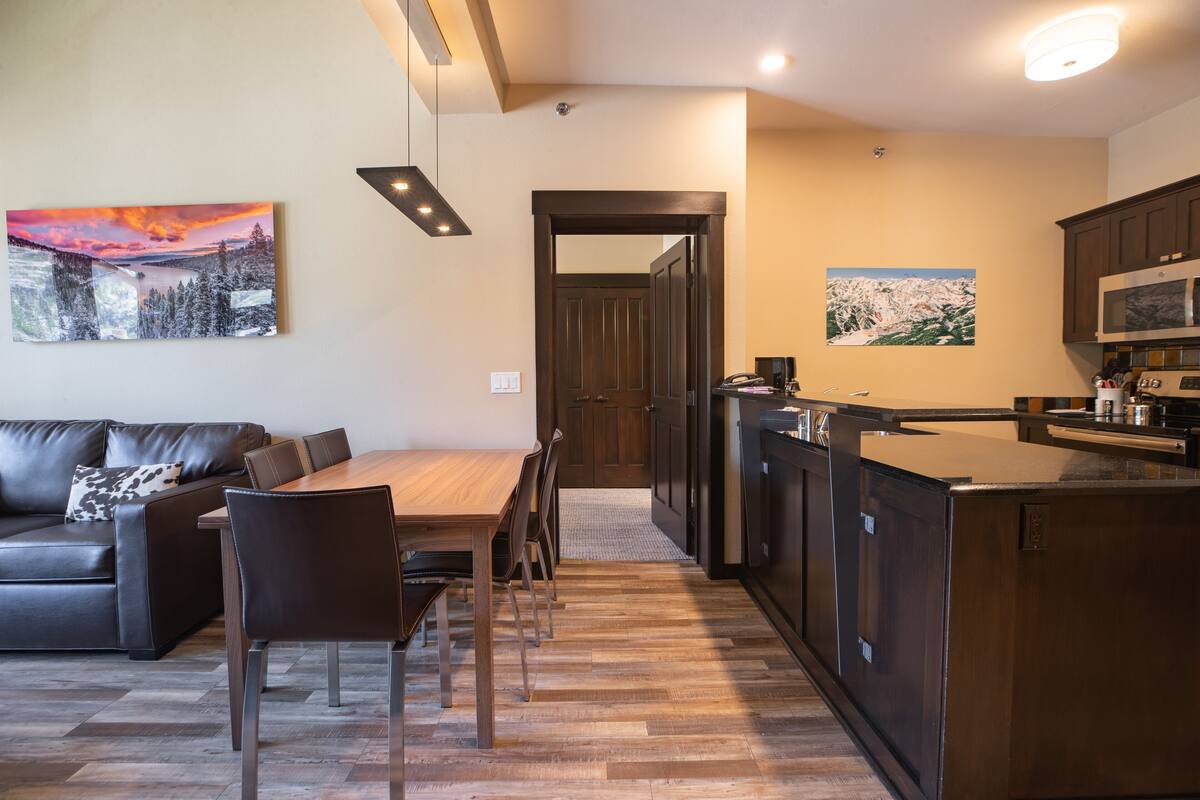 A modern kitchen with a wooden island, dark cabinetry, and a dining area with a wooden table and chairs.