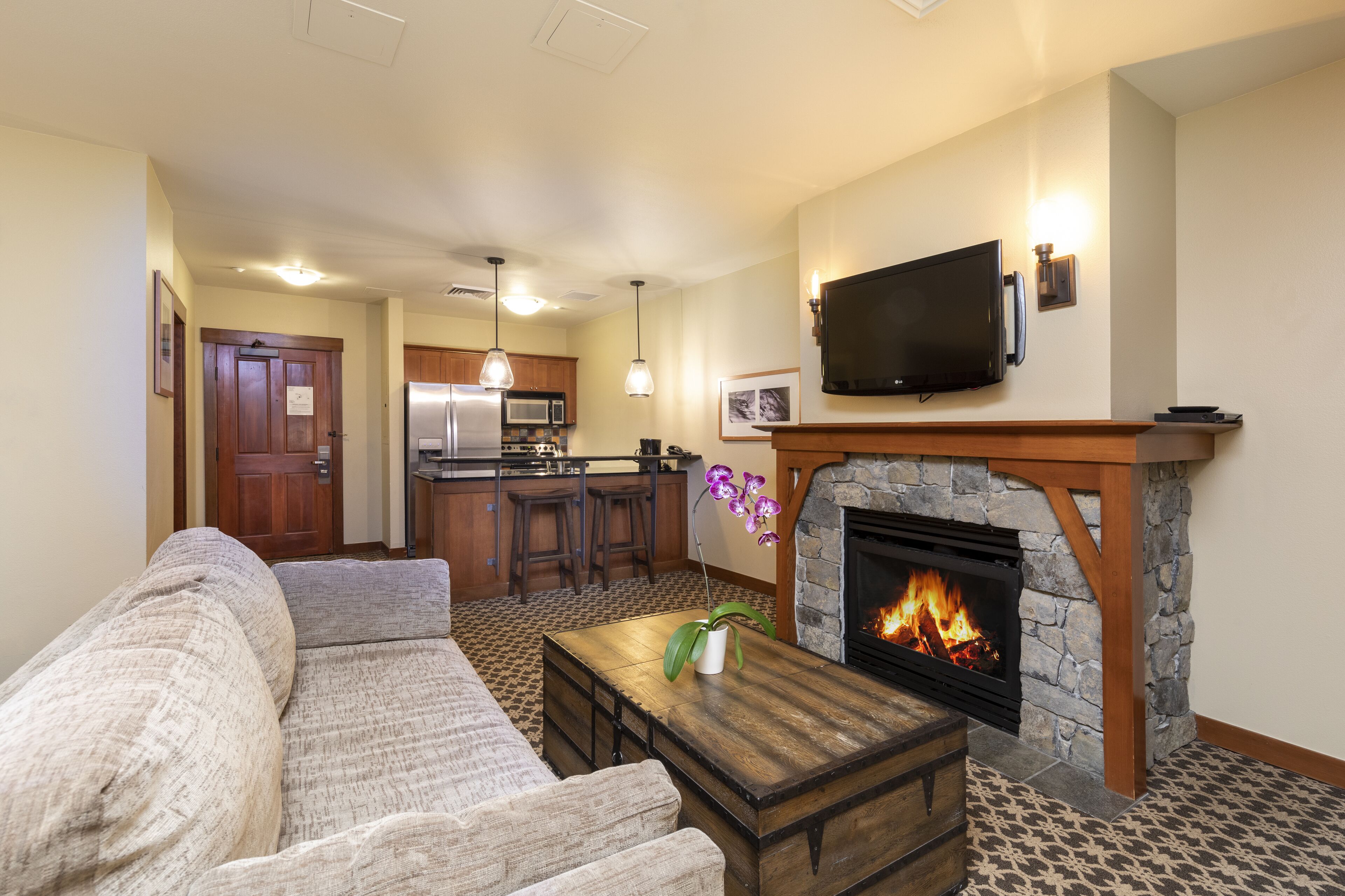 A living room with a fireplace, a sofa, a coffee table, and a kitchen in the background.
