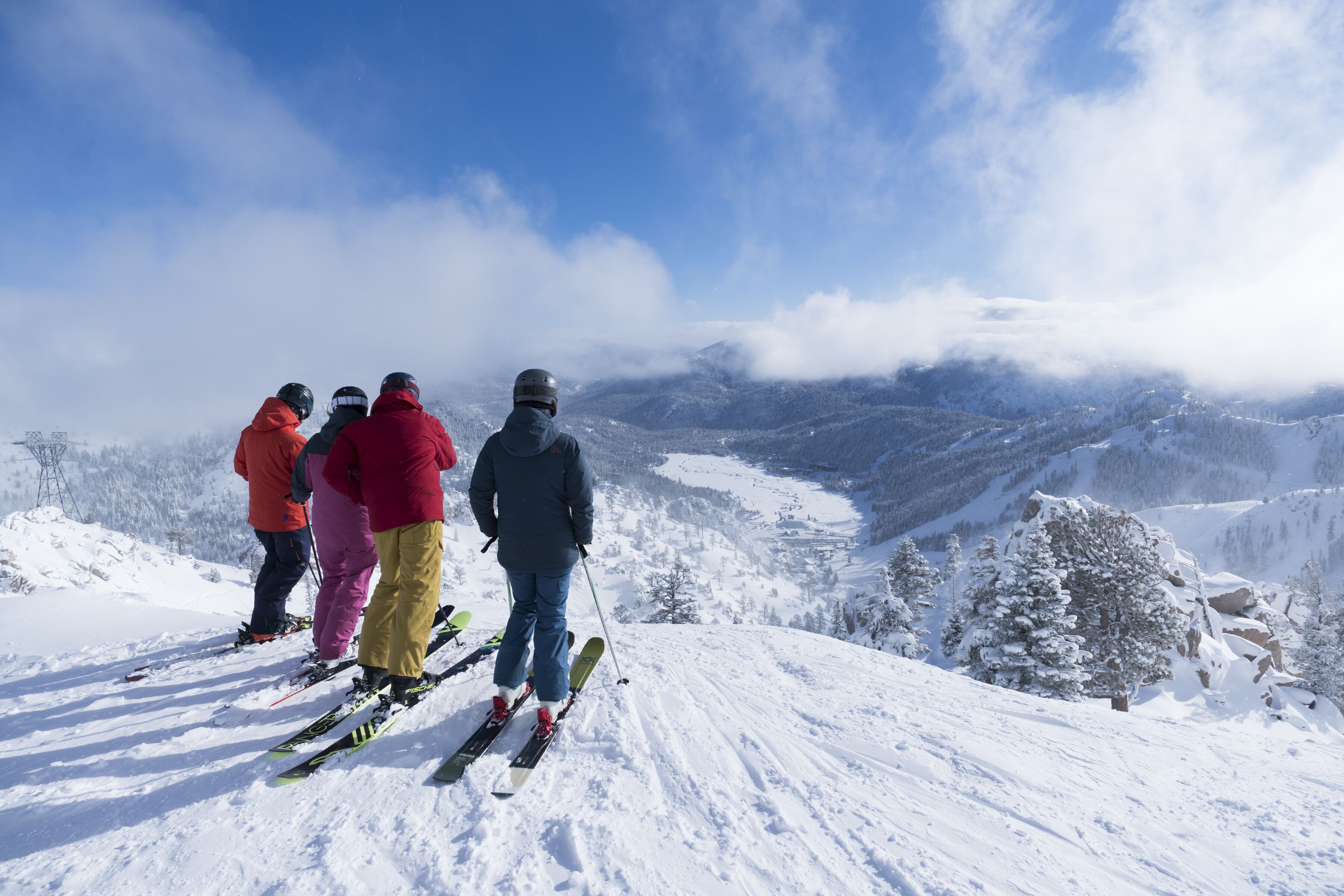 A group of skiers on a snowy mountain slope with a clear view of the valley below.