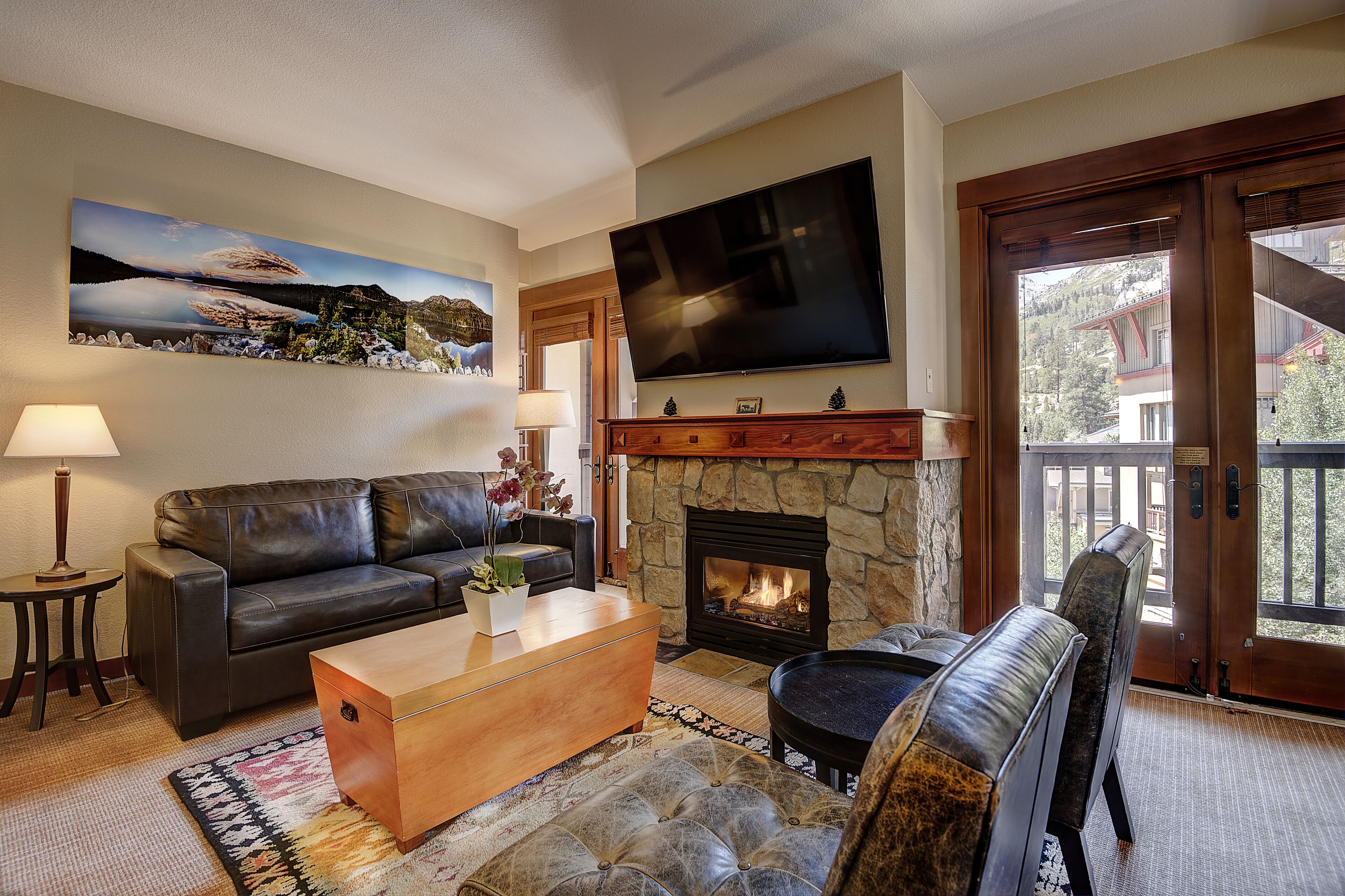 Una sala de estar con chimenea, un sofá, una mesa de centro, un televisor montado en la pared y vistas a través de un ventanal.