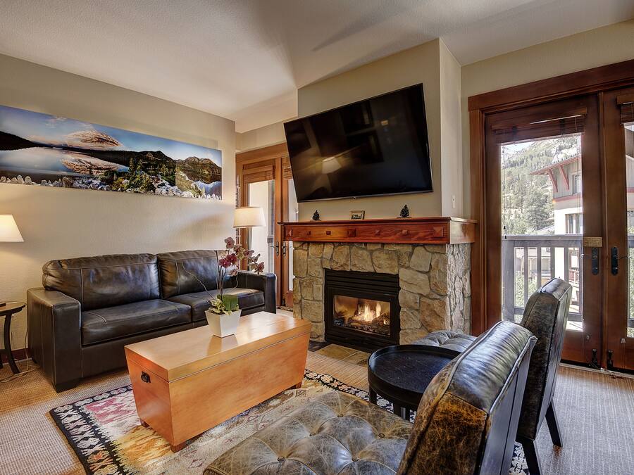 Una sala de estar con chimenea, un sofá, una mesa de centro, un televisor montado en la pared y vistas a través de un ventanal.