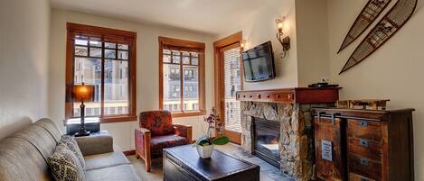 A cozy living room with a sofa, a coffee table, a fireplace, and a television mounted on the wall.