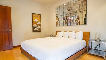A neatly made bed with white linens, a wooden headboard, a bedside table with a lamp, and a wall-mounted mirror.