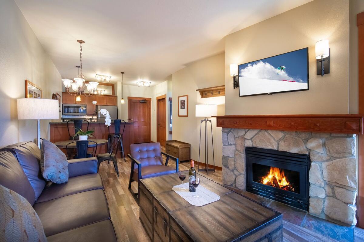 A living room with a stone fireplace, a television mounted above it, and a dining area in the background.