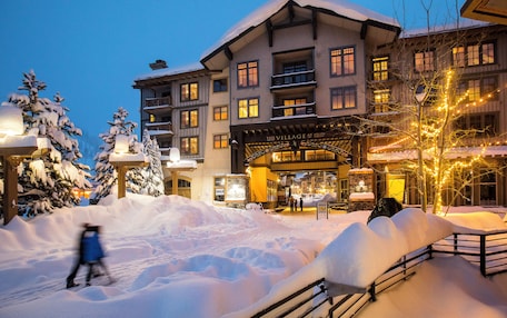 A snow-covered building with multiple balconies and a lit entrance.