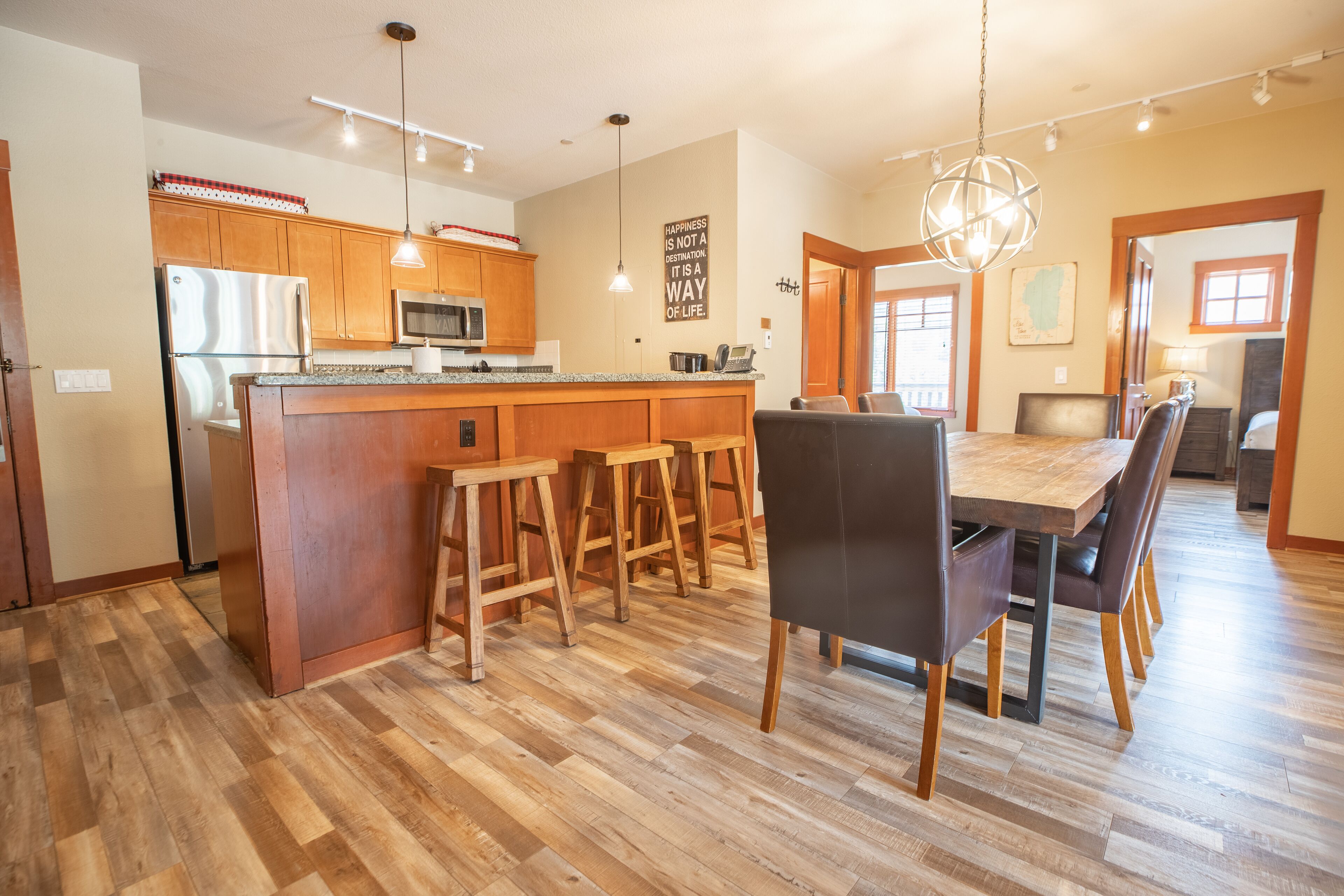 A modern kitchen with wooden cabinets, a central island, bar stools, and a dining area with a large table and chairs.