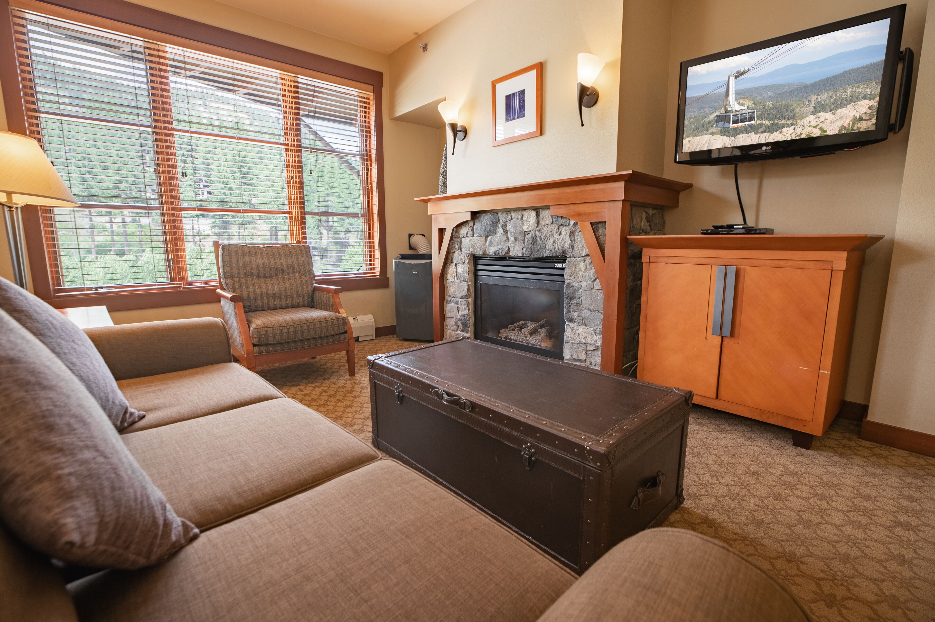 A living room with a fireplace, a television, and a large window with blinds.