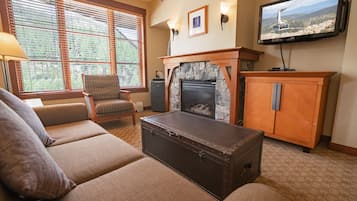 A living room with a fireplace, a television, and a large window with blinds.