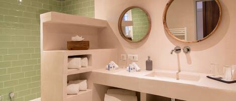 Un baño con un tocador color beige, dos espejos redondos, una zona de ducha con azulejos verdes y toallas dobladas con cuidado.
