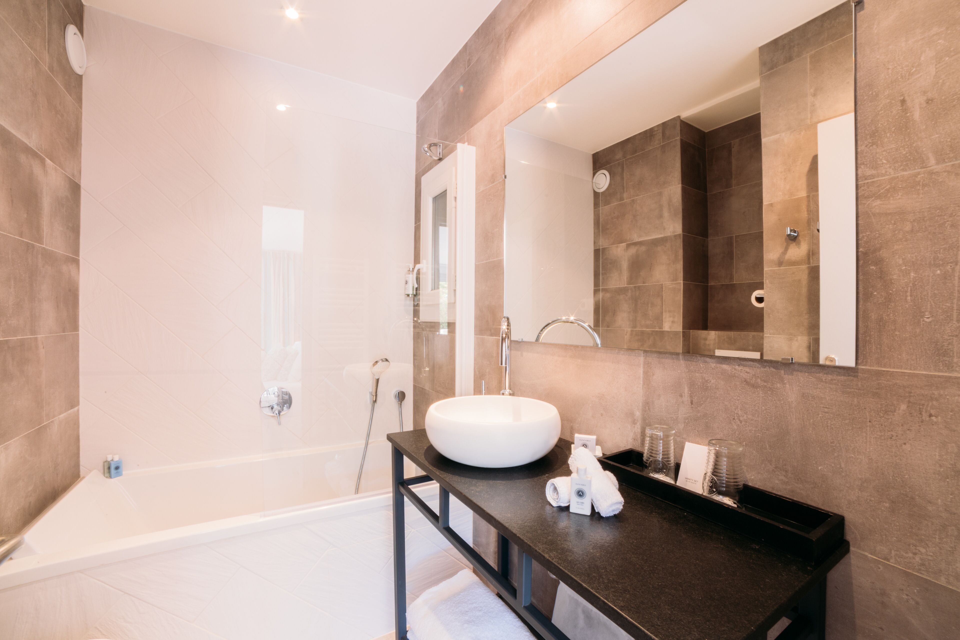 A modern bathroom with a large bathtub, a round sink, and a dark countertop.