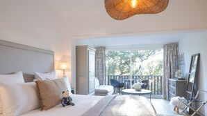 Quarto de hotel com uma cama grande, varanda com mesa e cadeiras, e vista para árvores.