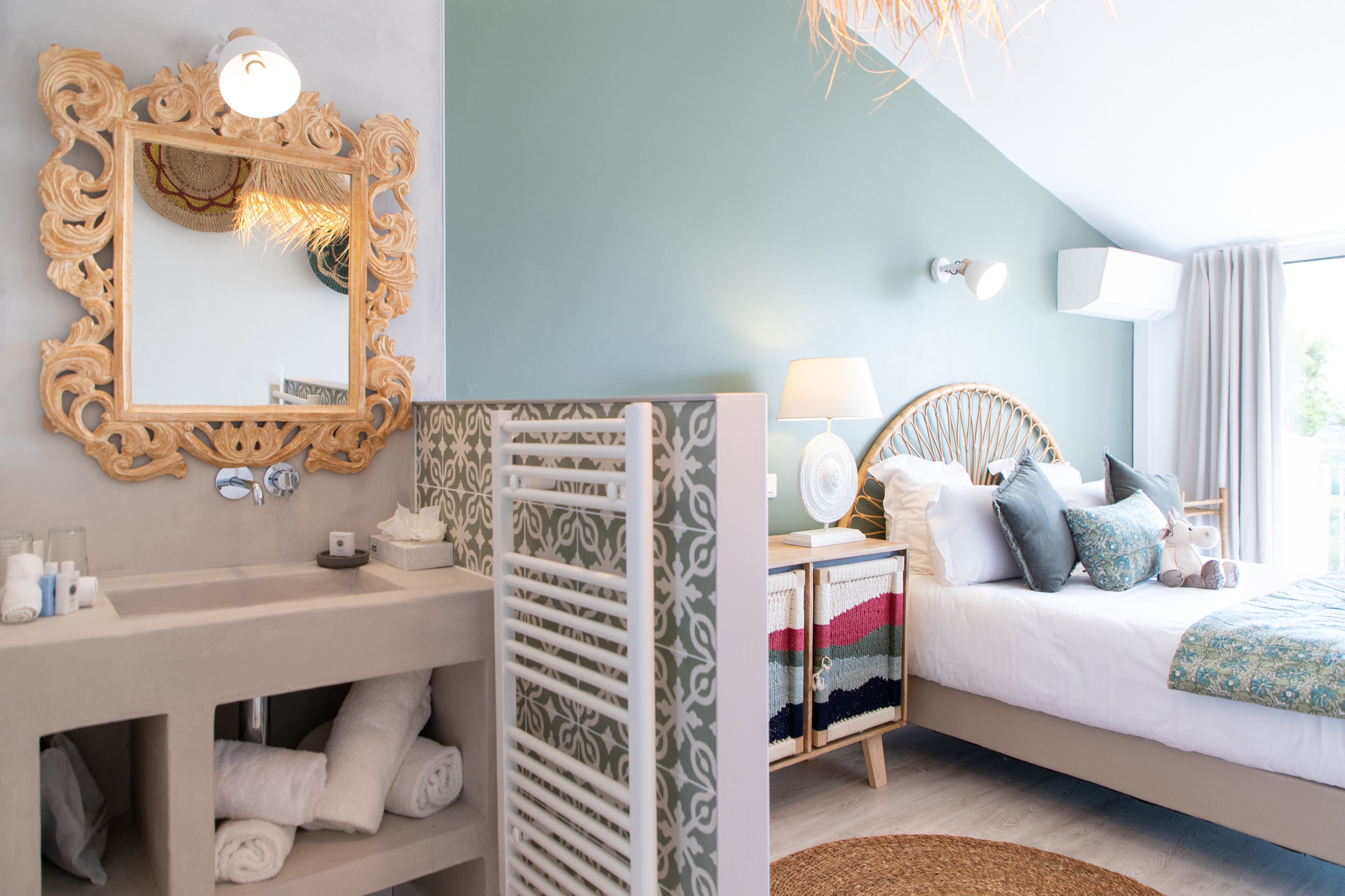 Un dormitorio con cama, mesita de noche, lámpara y un espejo con marco decorativo.