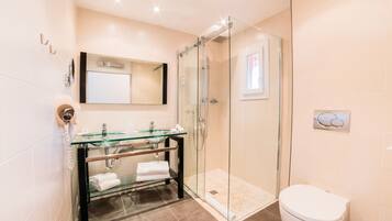 A modern bathroom with a glass shower enclosure, a glass sink, and a toilet.