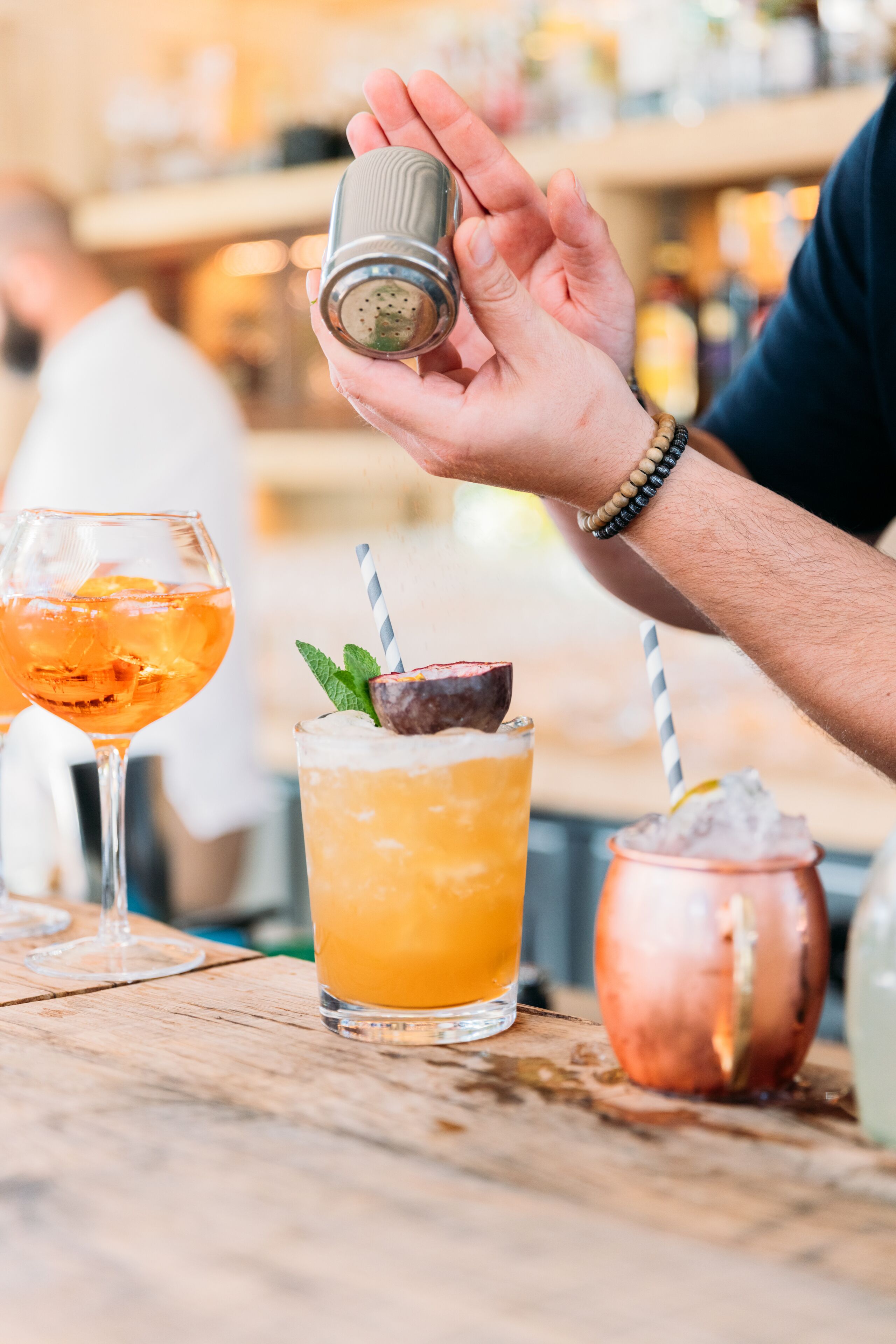 Une main tenant un saleroisier au-dessus d’un verre contenant une boisson à l’orange, décorée d’une feuille de menthe et munie d’une paille.