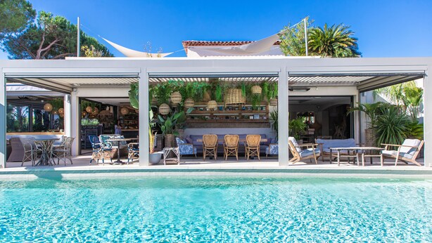 Área de piscina com espaço coberto para sentar, cadeiras de descanso e um bar.