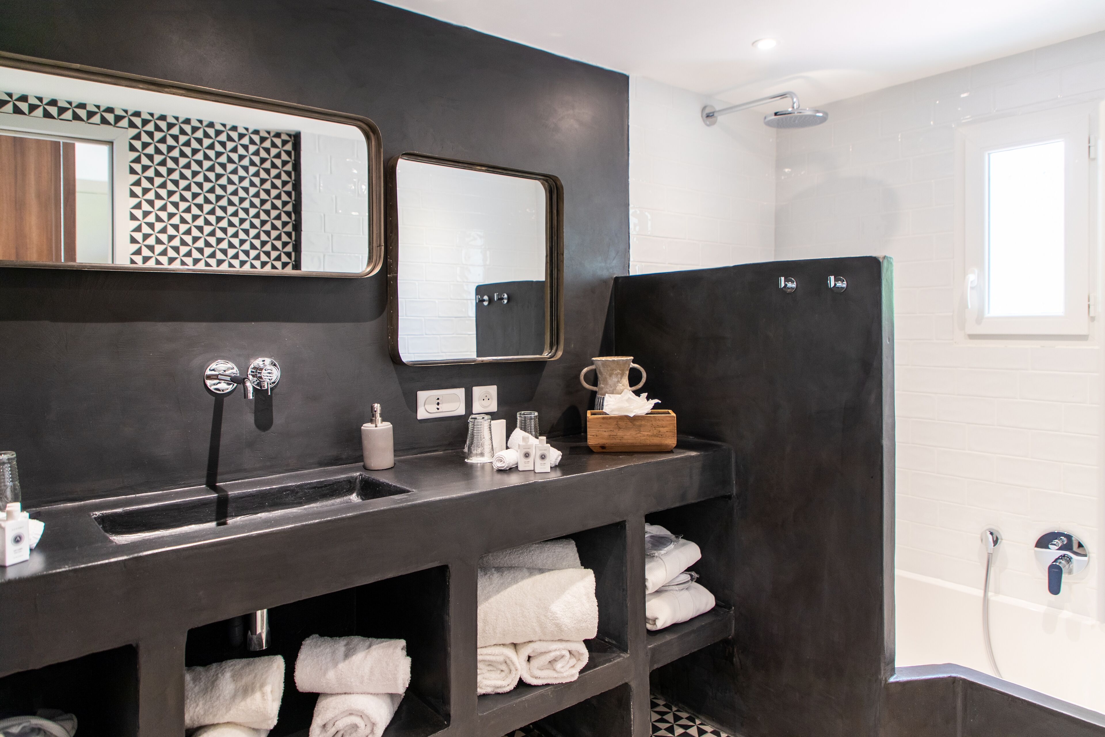 A modern bathroom with a dark vanity, a large mirror, a shower area, and neatly folded towels.