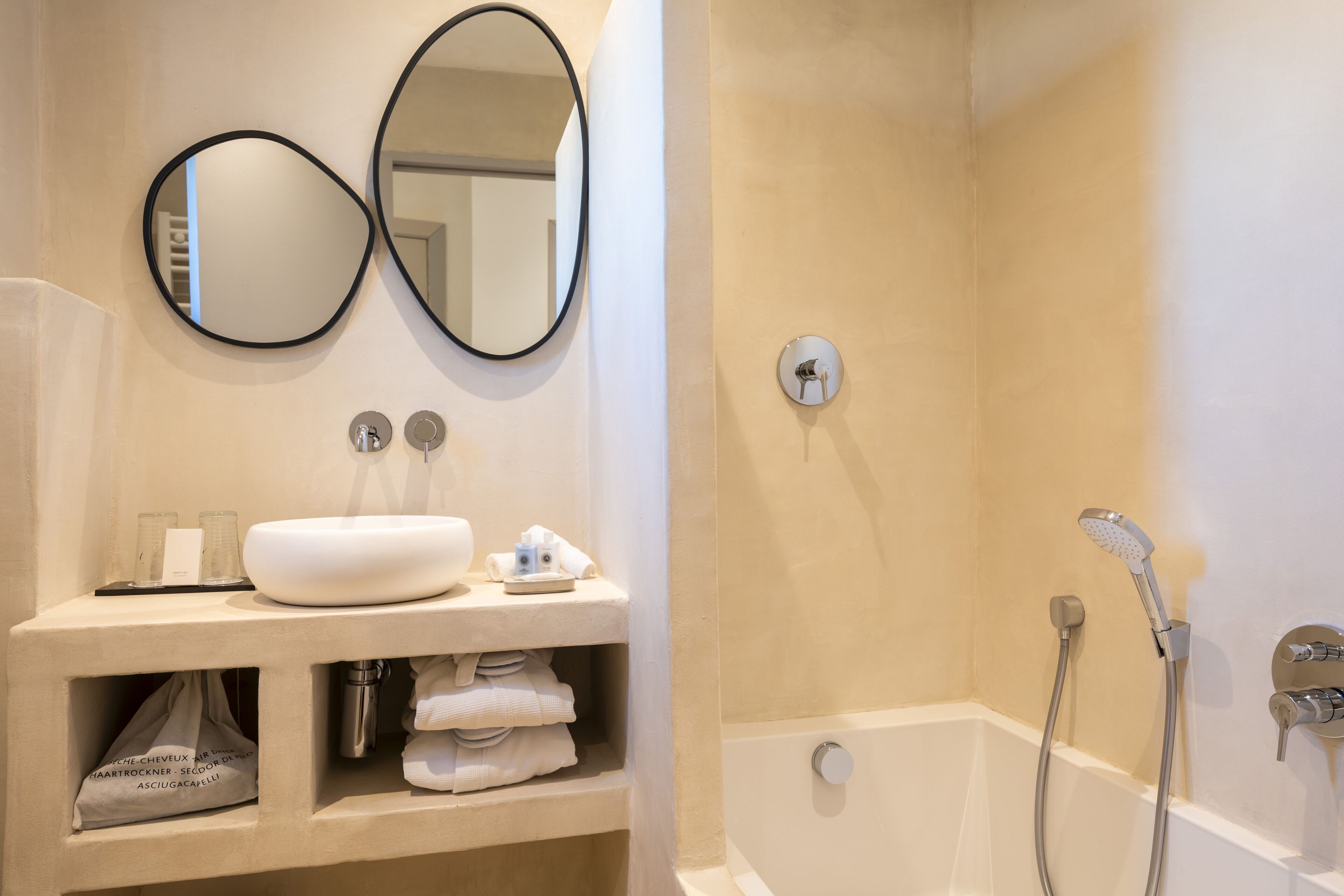 A bathroom with a white sink, two mirrors, a towel rack, and a shower area.