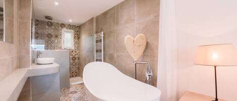 A modern bathroom with a freestanding bathtub, a vanity with a sink, and a heart-shaped mirror.