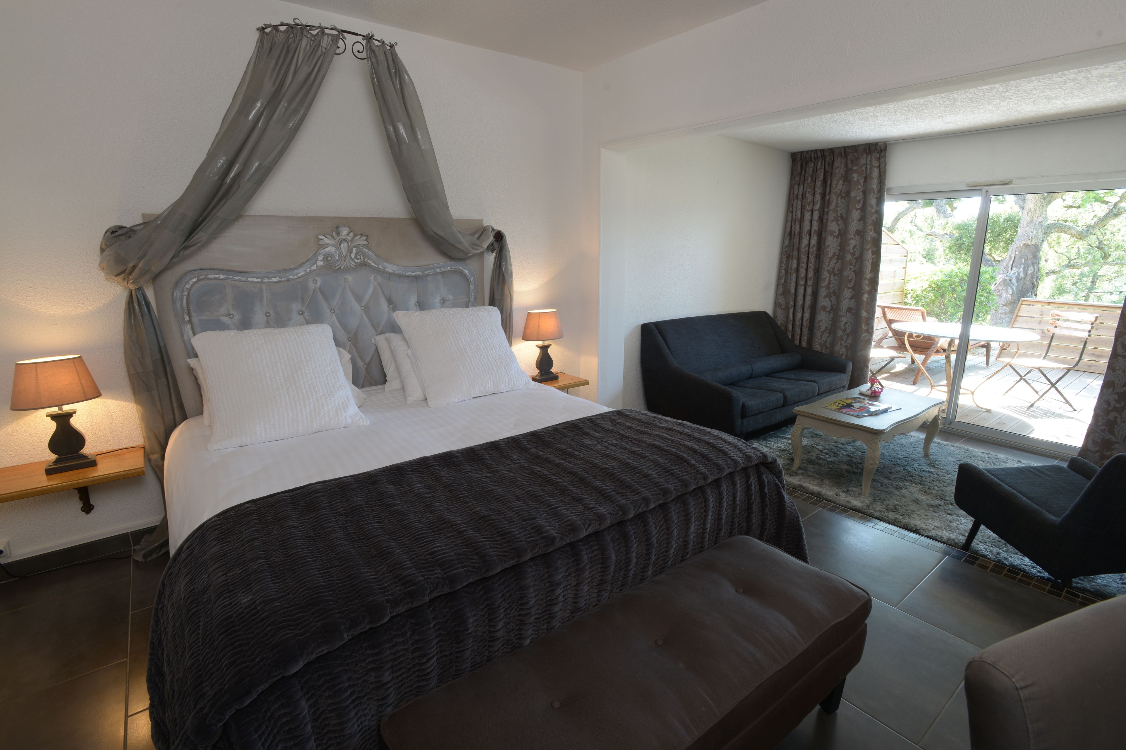 Quarto com cama de dossel, área de estar com poltrona e mesa, e vista para o exterior.
