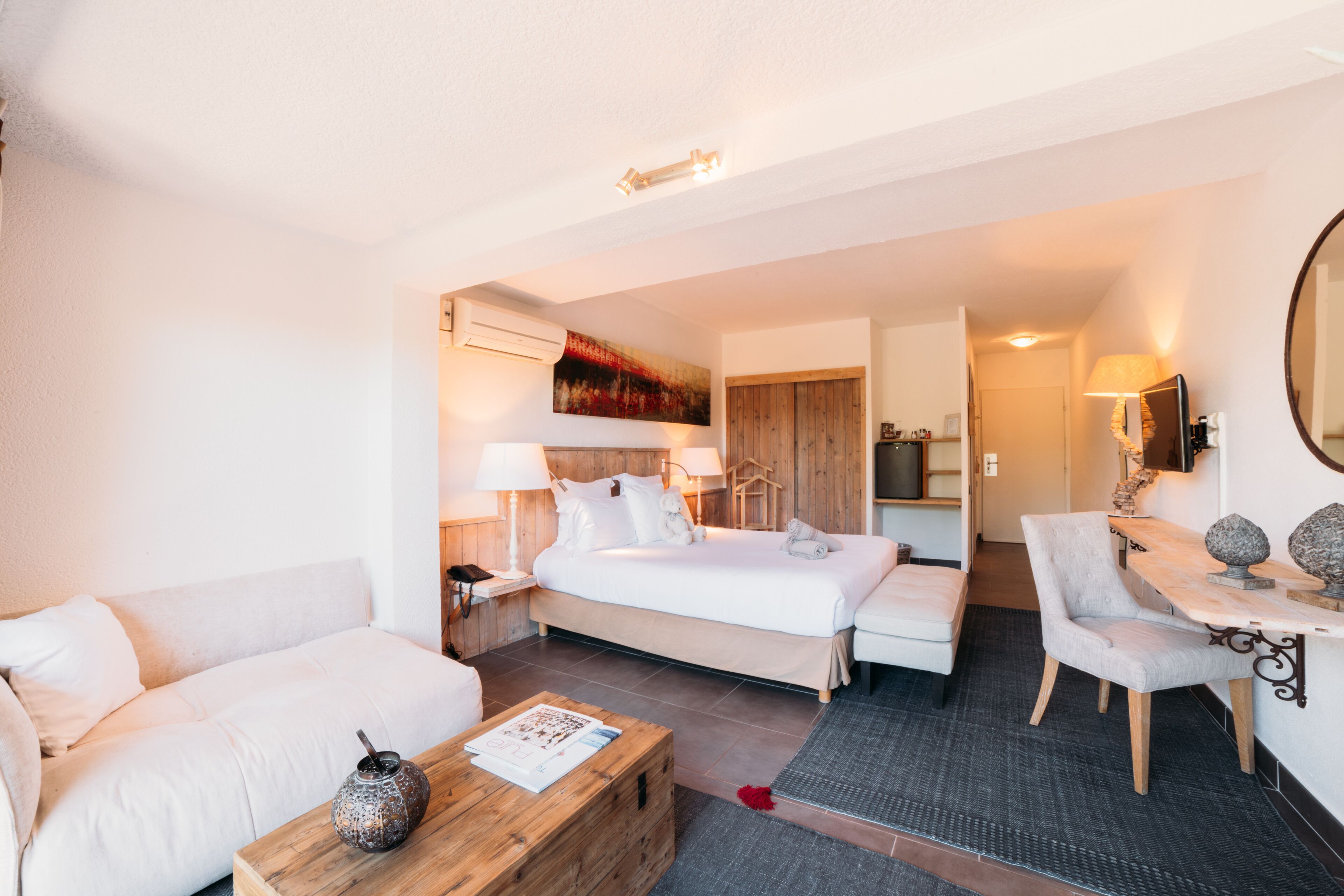 Ein Hotelzimmer mit einem Bett, einem Sofa, einem Holztisch und einem Schreibtisch mit Lampe.