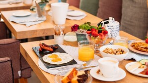 Disposição de café da manhã com diversos pratos, incluindo ovos, frutas e doces, sobre uma mesa de madeira.