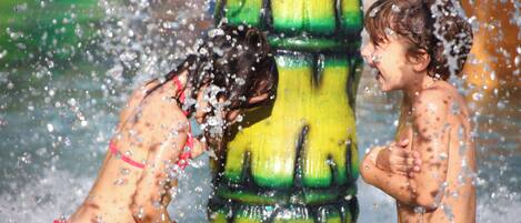 Two children playing in water, with a large yellow and green structure in the background.
