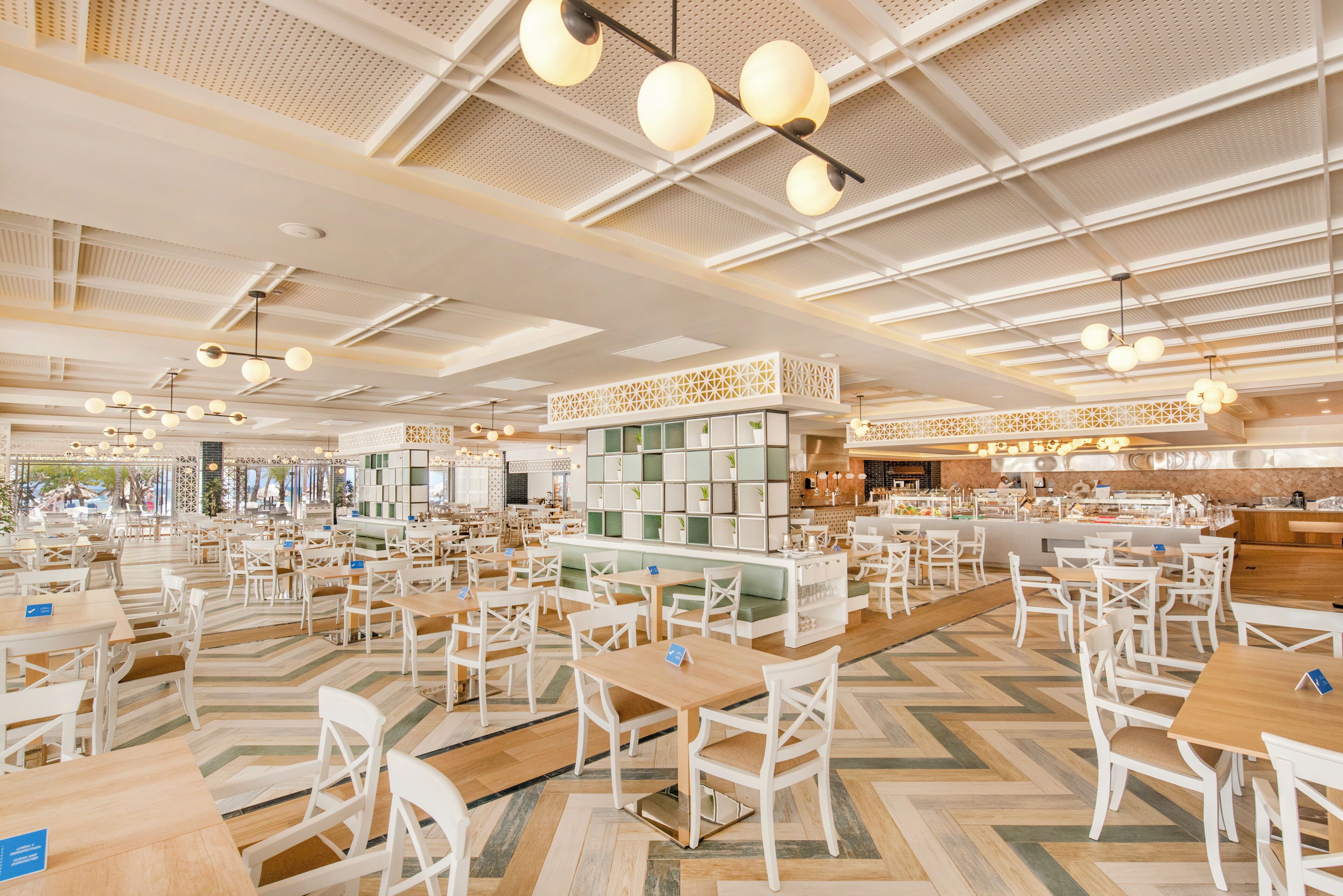 A spacious restaurant with multiple dining areas, high ceilings with hanging lights, and a modern interior design.