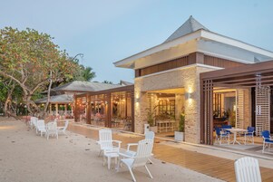 Un restaurante frente a la playa con terraza al aire libre, fachada de piedra y zona de patio techada.