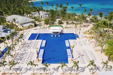 A resort with a central swimming pool, sun loungers, and palm trees.