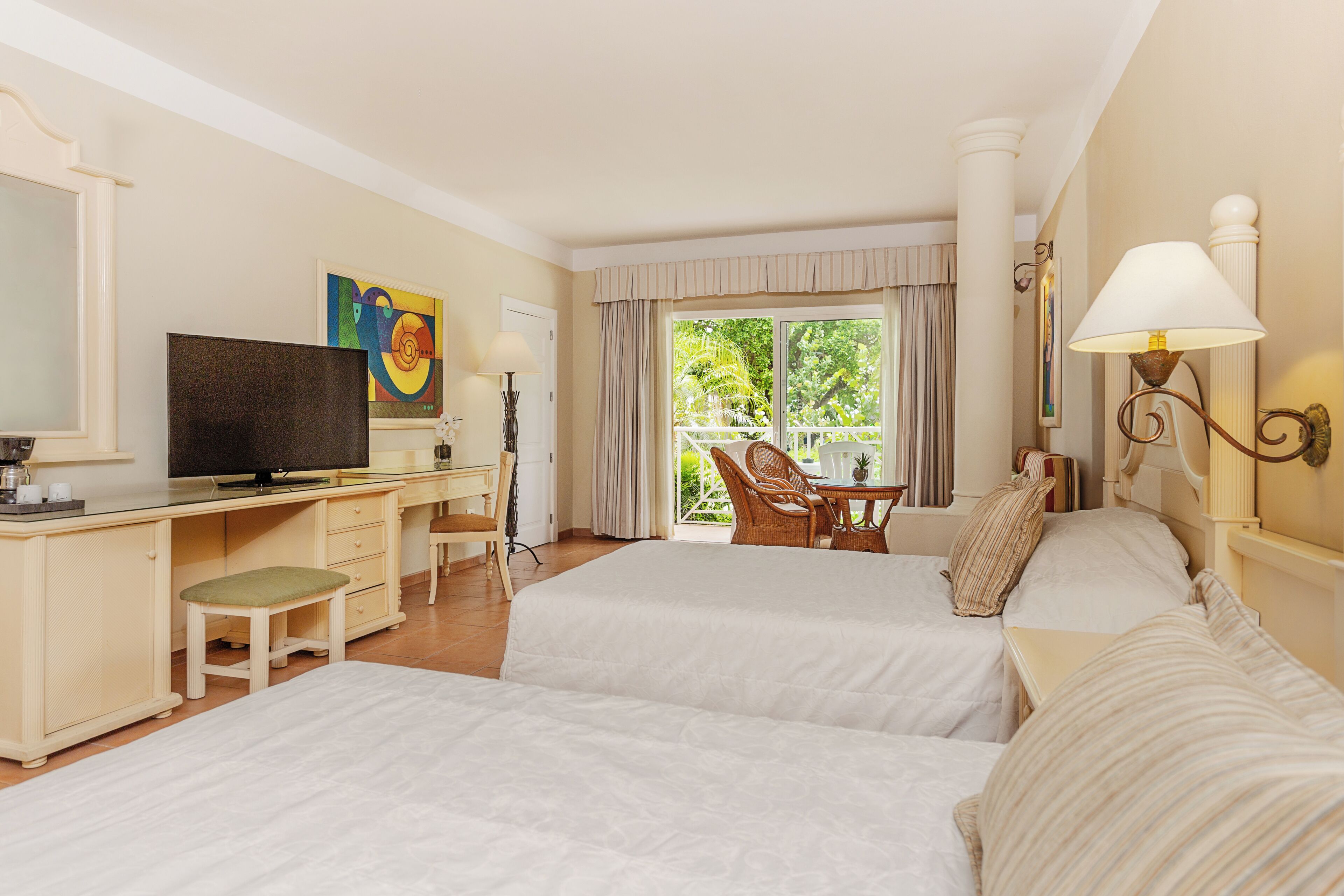 Habitación de hotel con dos camas, un escritorio, televisor, una silla y vista a zonas verdes por la ventana.