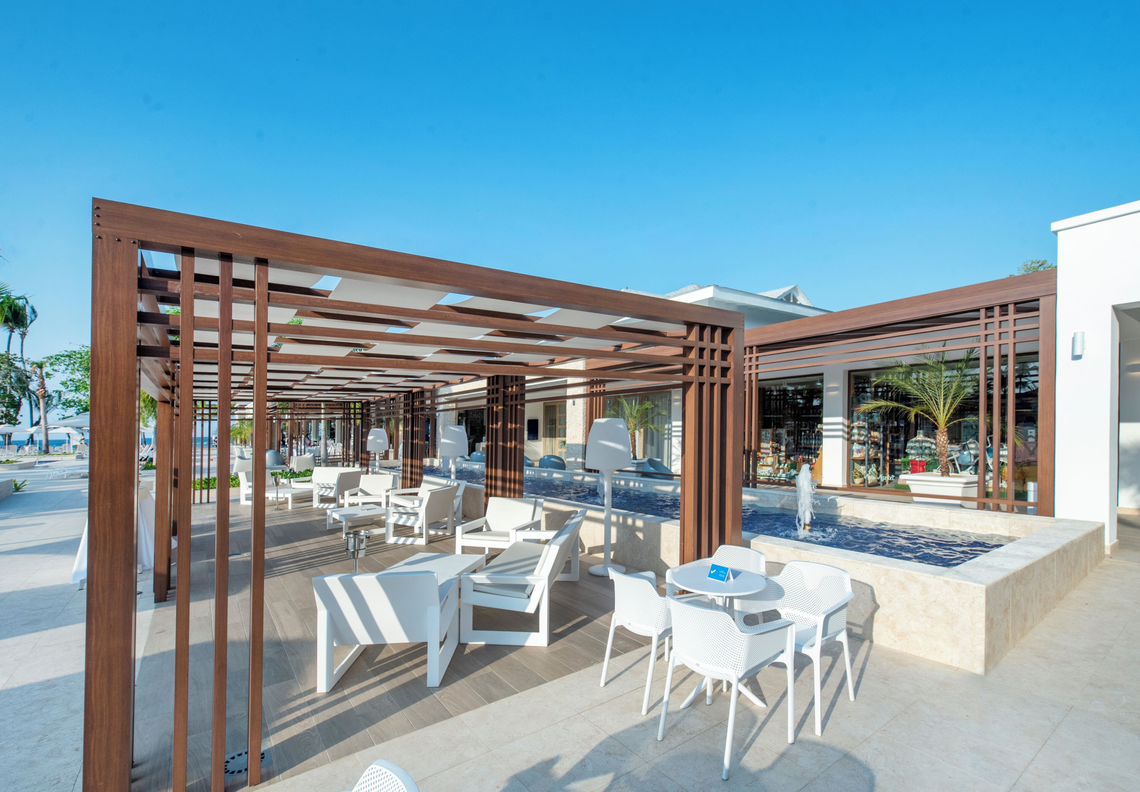 Un patio al aire libre con mobiliario blanco, una piscina y un edificio moderno de fondo.