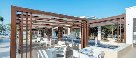 Un patio al aire libre con mobiliario blanco, una piscina y un edificio moderno de fondo.