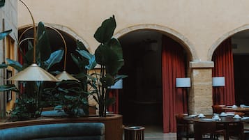 Eine großzügige Lobby mit hoher Decke, ausgestattet mit einer zentralen Sitzecke mit Sofa und Tischen, umgeben von großen Kübelpflanzen und einem gemusterten Boden.